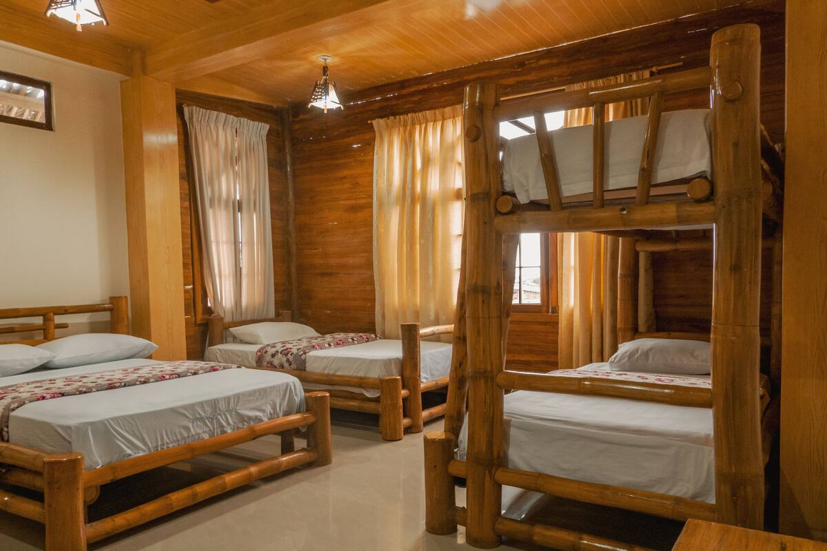 A cabin-style room with four wooden bunk beds, a wooden table, and a ceiling light fixture.