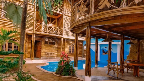 A wooden cabin-style building with a pool, outdoor seating, and tropical plants. - Hostal Poseidon (Puerto Cayo)