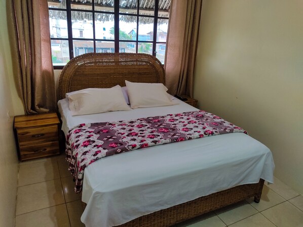A bed with a floral bedspread, a wooden nightstand, and a window with curtains.