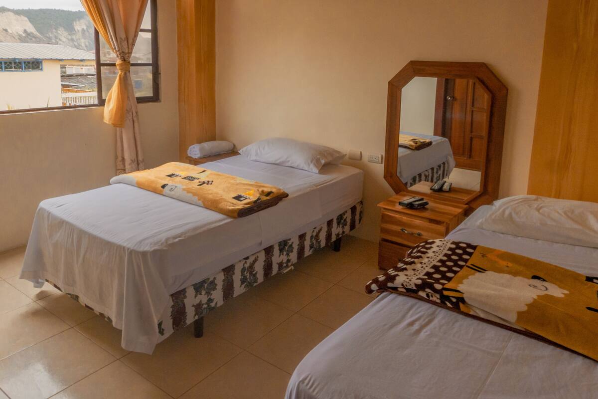 A hotel room with two single beds, a wooden nightstand with a mirror, and a window with curtains.