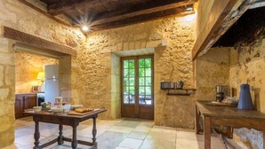 A rustic kitchen with stone walls, a wooden table, and a window with a view of greenery. - Chateau Rochette - Four Bedroom Castle, Sleeps 8 (Mauzens-et-Miremont)