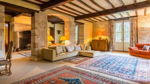 A cozy living room with a stone fireplace, a sofa, a red armchair, and patterned rugs. - Chateau Quercy - Seven Bedroom Castle, Sleeps 15 (Castelsagrat)