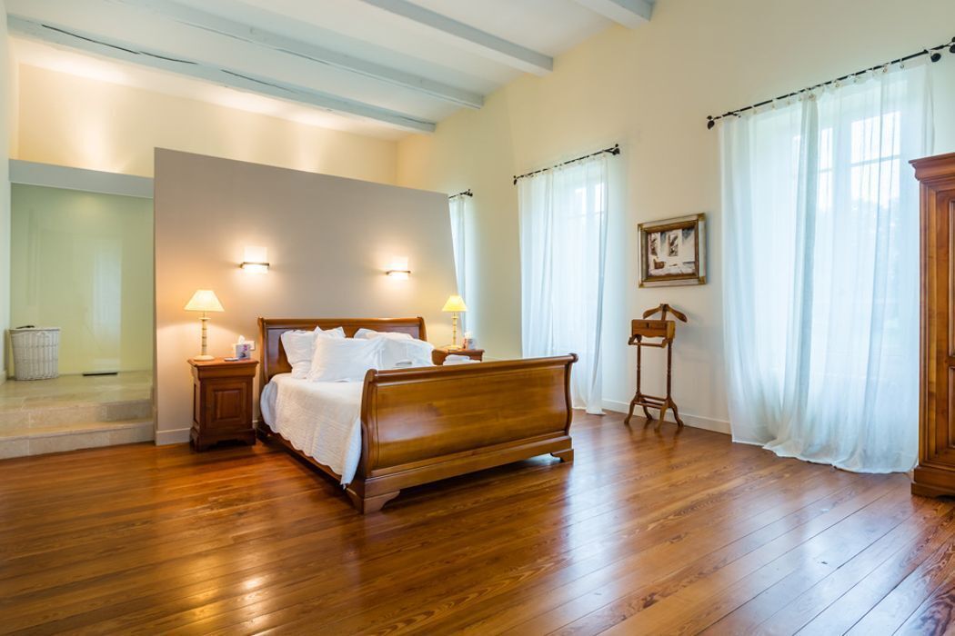 A spacious bedroom with a wooden bed, two bedside lamps, a nightstand, and a wooden wardrobe.