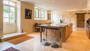 A modern kitchen with a bar area, large windows, and a stone accent wall. - Chateau Quercy - Seven Bedroom Castle, Sleeps 15 (Castelsagrat)