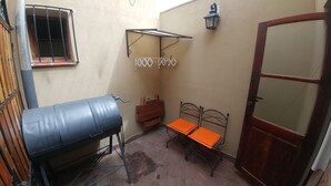 Une petite pièce fermée, dotée d’une grille métallique, d’une porte en bois, d’un cadre de lit en métal avec un matelas orange, d’une petite table et d’un étendoir fixé au mur.