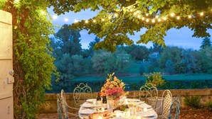 An outdoor dining area with a table set for two, surrounded by metal chairs, under a tree with string lights. - Villa Du Fleuve - Four Bedroom Villa, Sleeps 8 (Flaujagues)