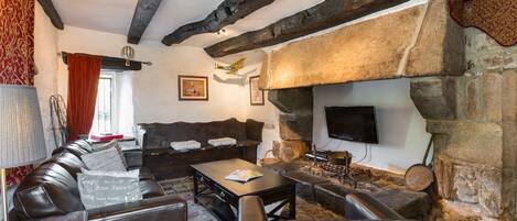 A cozy living room with a stone fireplace, leather sofas, and a flat-screen TV mounted on the wall.