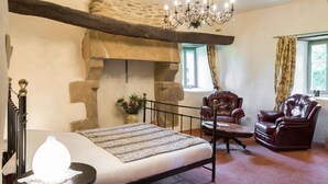 Una habitación con chimenea de piedra, una cama con manta estampada, sillones de cuero y un candelabro.