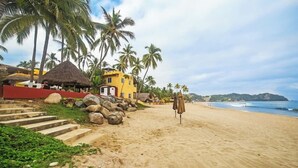 Ein Strand mit einem gelben Gebäude, Palmen und einem Gebäude mit einem Reetdach.