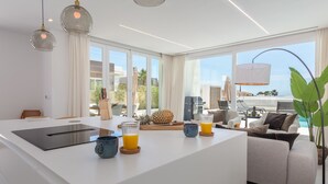 Eine moderne Küche mit einer großen Kochinsel, einem Essbereich mit Sofa und Tisch sowie Blick ins Freie.