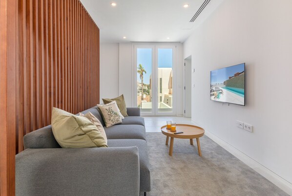 A modern living room with a grey sofa, wooden panel wall, and a painting of a coastal scene. - Modern Villa with Private Pool & Rooftop Terrace (Mijas Costa)