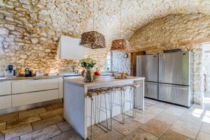 Une cuisine aux murs en pierre, dotée d’appareils électroménagers en acier inoxydable et d’un îlot central agrémenté de tabourets de bar.