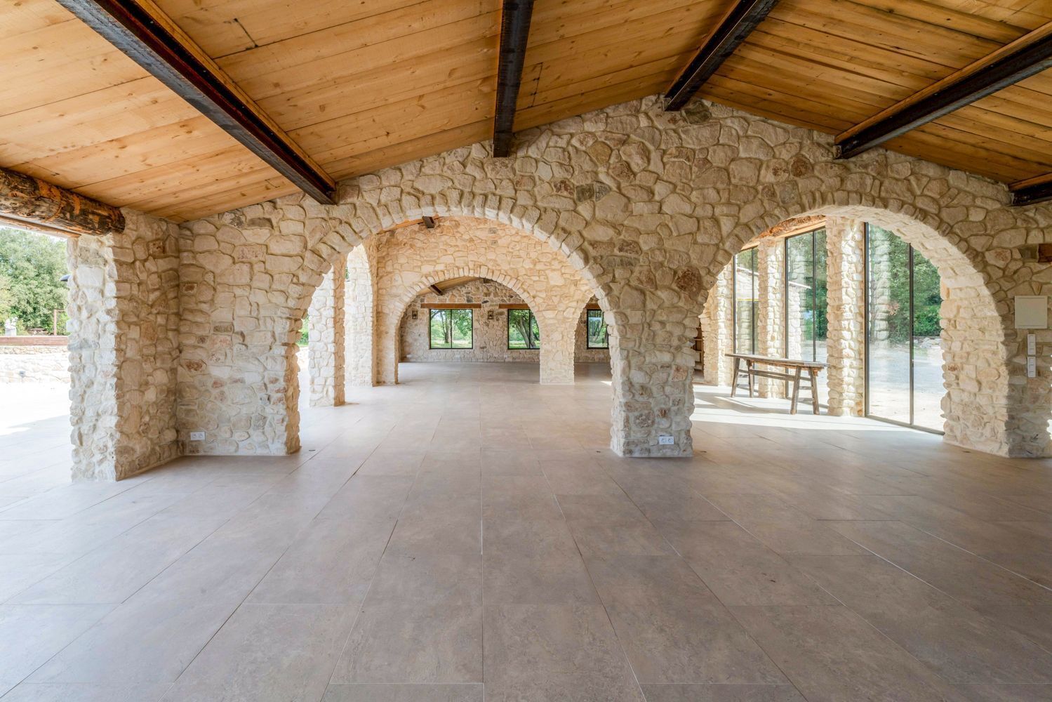 A spacious interior with stone arches and a wooden ceiling, featuring a bench and a table.