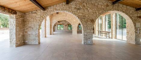 A spacious interior with stone arches and a wooden ceiling, featuring a bench and a table.
