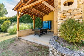 Un espace extérieur aménagé avec une table de billard, une pergola en bois, un mur en pierre et un meuble bleu.