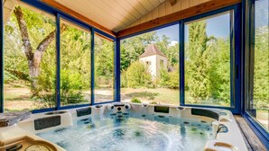 A hot tub in a room with large windows overlooking a garden and a small tower structure. - Les Cypres - Three Bedroom Villa, Sleeps 6 (Vézac)