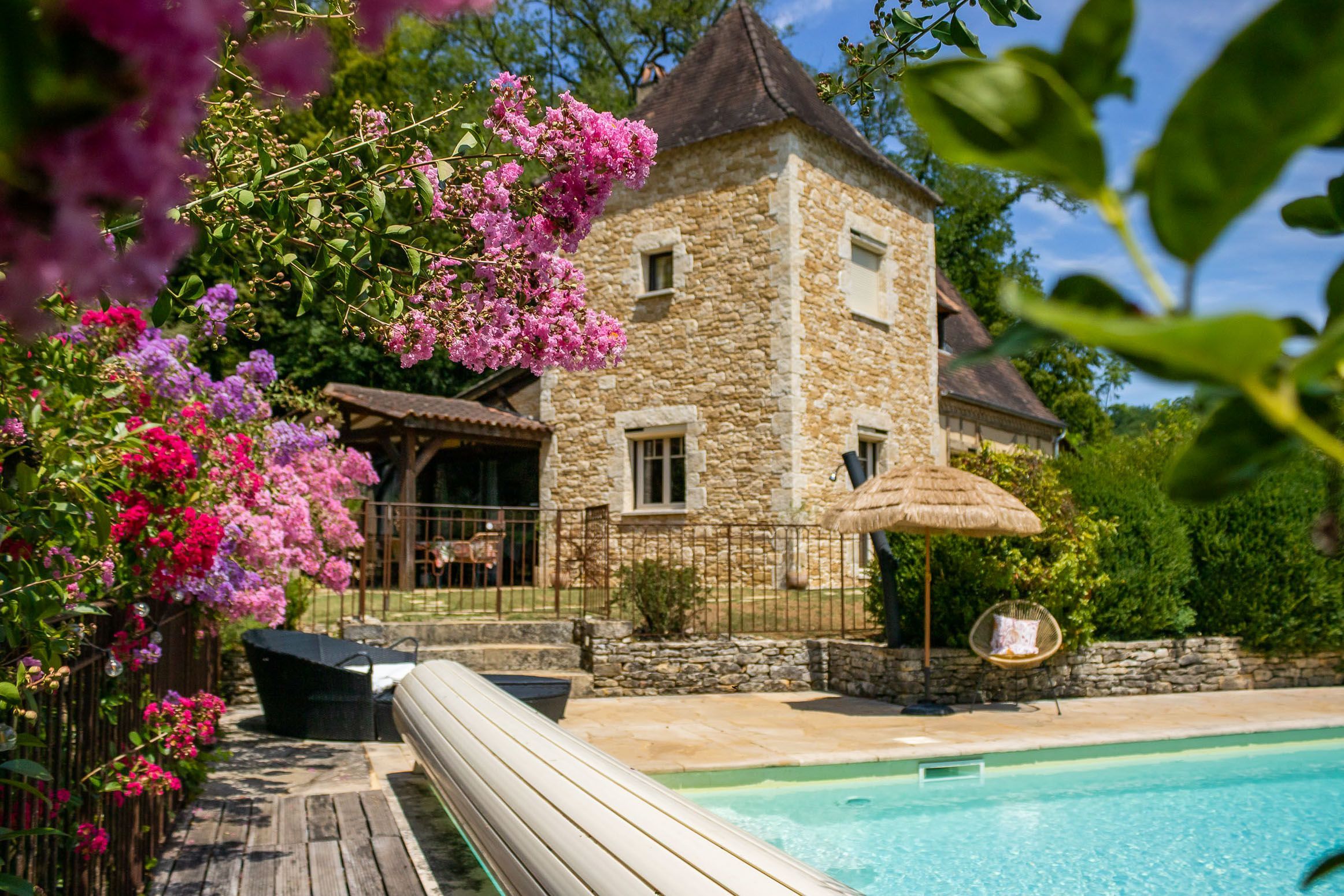 A stone building with a pool, surrounded by lush greenery and flowering plants.