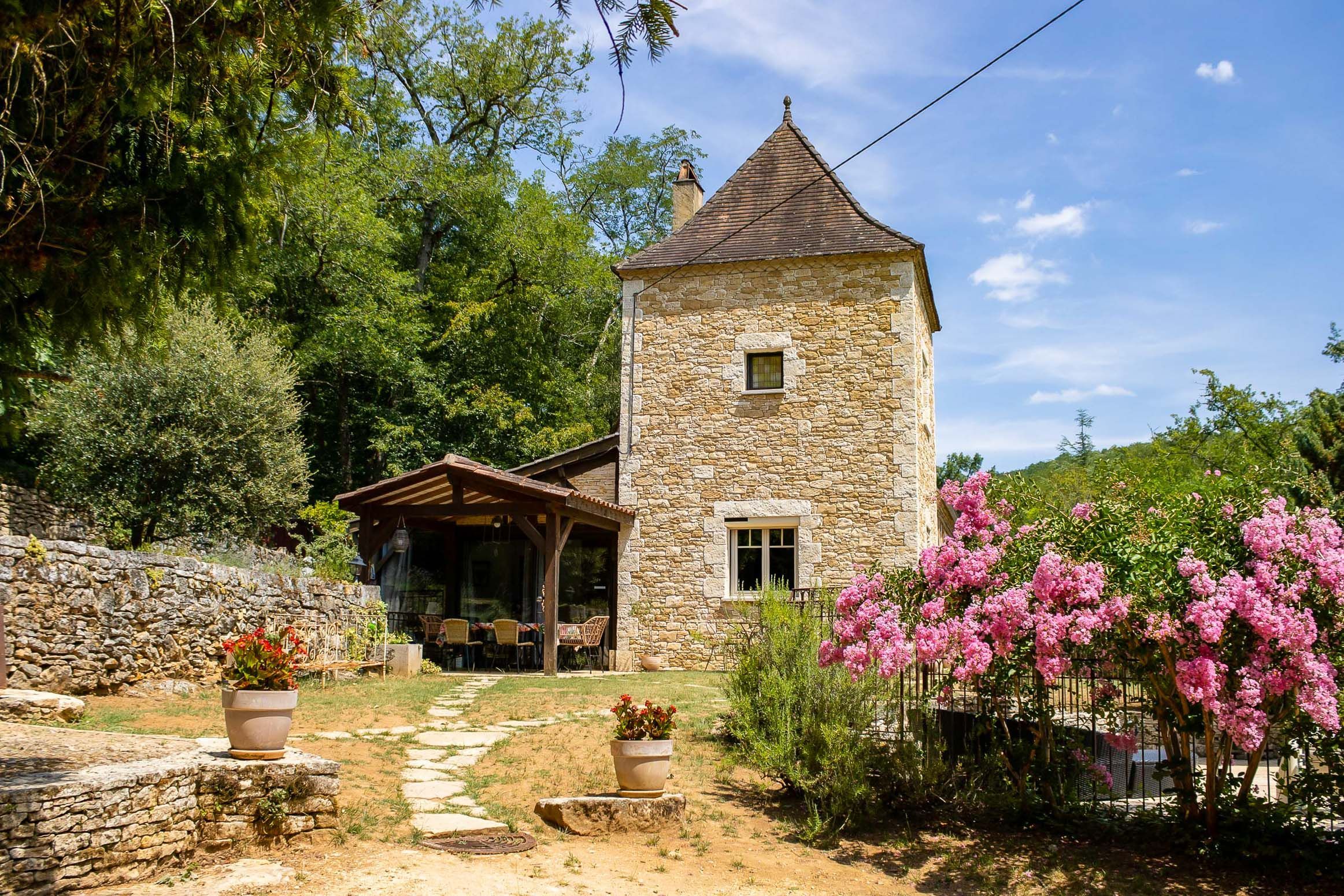 Una torre de piedra con techo a dos aguas, rodeada de abundante vegetación y plantas en flor.