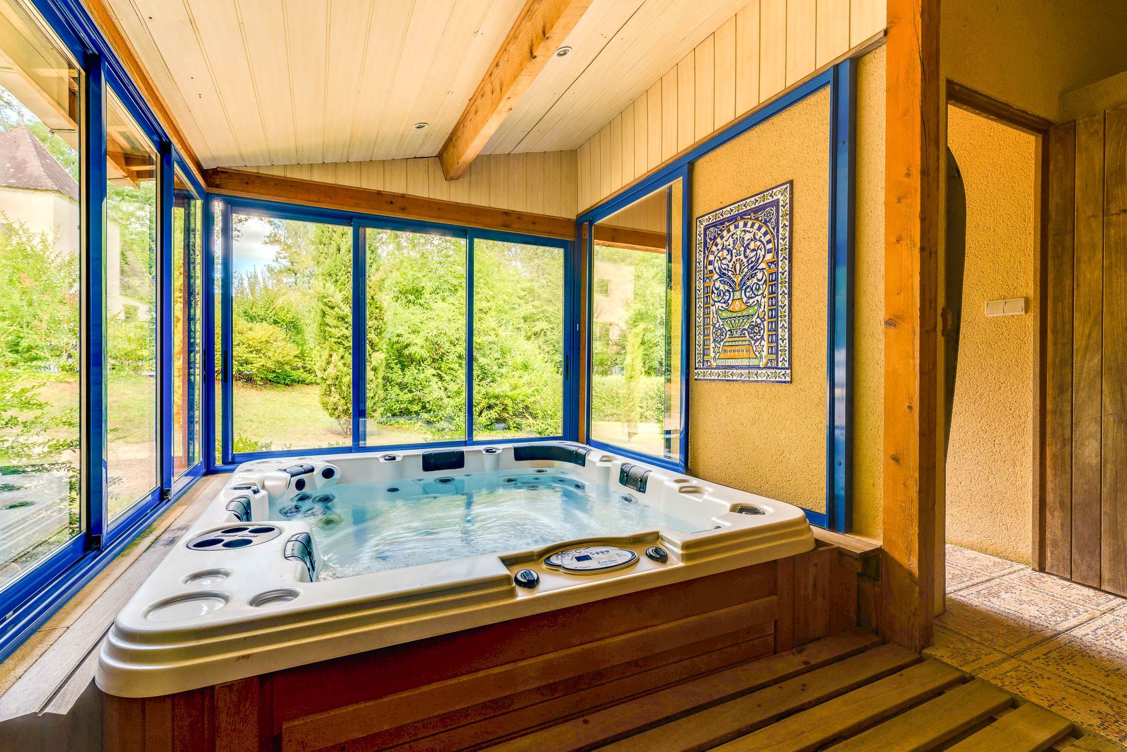 A hot tub with a view of a garden through large windows.