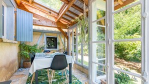 A cozy dining area with a table set for two, surrounded by large windows offering a view of the garden. - Les Cypres - Three Bedroom Villa, Sleeps 6 (Vézac)