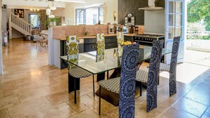 A spacious kitchen with a central island, modern appliances, and a dining area with patterned chairs and a glass table. - Villa Juno - Four Bedroom Villa, Sleeps 8 (Moncrabeau)