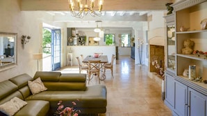 A spacious living room with a green sofa, a dining area with a table and chairs, and a kitchen in the background. - Villa Juno - Four Bedroom Villa, Sleeps 8 (Moncrabeau)