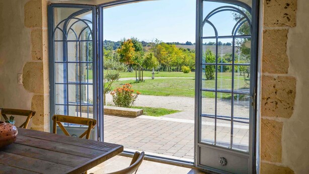 A room with a wooden table and chairs, a large arched window, and a view of a garden. - Villa Juno - Four Bedroom Villa, Sleeps 8 (Moncrabeau)
