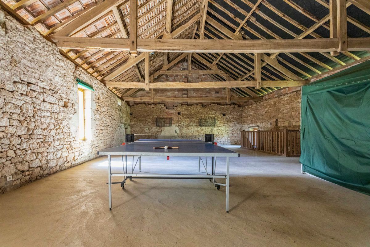 Una mesa de ping pong en una habitación rústica con paredes de piedra y vigas de madera.