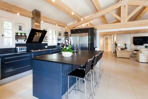 Eine moderne Küche mit einer zentralen Kochinsel, Barhocker und einem Essbereich inklusive Sofa und Fernseher.
