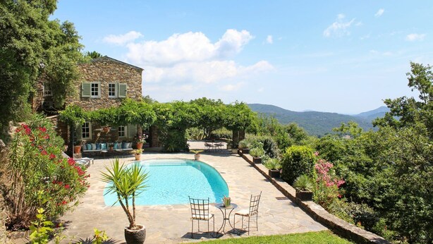 Una casa in pietra con piscina, immersa nel verde lussureggiante e con montagne sullo sfondo.