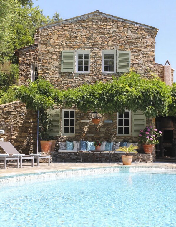 A stone building with a pool, outdoor seating, and a pergola with climbing plants.