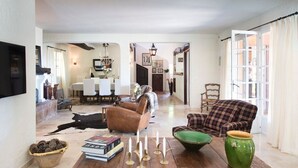 Un ampio soggiorno con pavimento in legno, una poltrona in pelle marrone, un divano a quadri e un'area pranzo illuminata da un lampadario.
