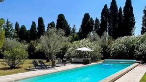 Une piscine rectangulaire dont le bord est revêtu de carreaux, entourée d’un espace patio aménagé avec des chaises longues et une table.