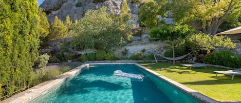 Ein rechteckiger Swimmingpool mit klarem, blauem Wasser, umgeben von üppiger Vegetation und einer felsigen Klippe im Hintergrund.