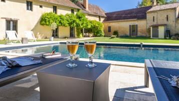 Un espace aménagé au bord de la piscine, avec des chaises longues et deux verres contenant une boisson, posés sur une table.