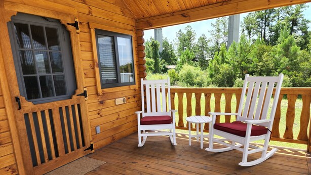 Eine Holzterrasse mit zwei Schaukelstühlen und einem kleinen Tisch, mit Blick auf eine bewaldete Gegend.