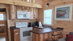 Ein Holzblockhaus-Interieur mit einer Küche, ausgestattet mit Herd, Mikrowelle und Toaster. Es gibt einen Essbereich mit Tisch und Stühlen sowie ein Sofa.