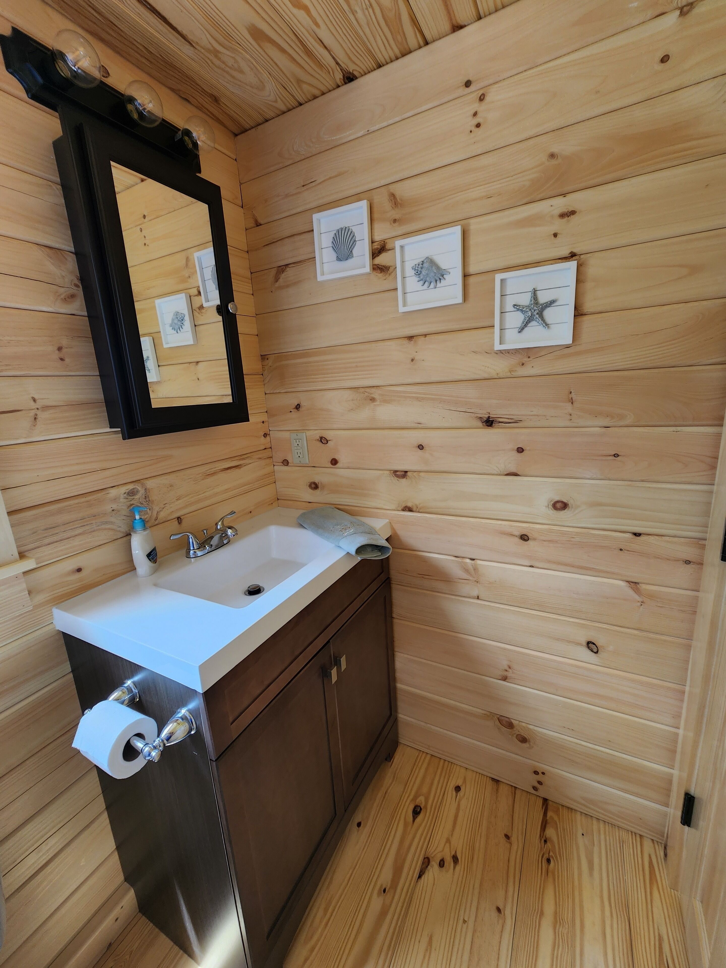 Ein Badezimmer mit Holzvertäfelung, einem Waschbecken, einem Spiegel und einem gerahmten Kunstwerk an der Wand.