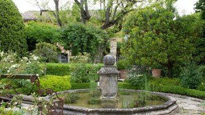 Un jardin agrémenté d’une fontaine circulaire, entouré de haies et d’arbres bien entretenus.