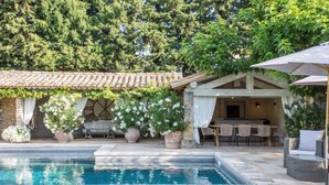 Un espace aménagé au bord de la piscine, avec un bâtiment en pierre, des sièges d’extérieur et des plantes en pot.