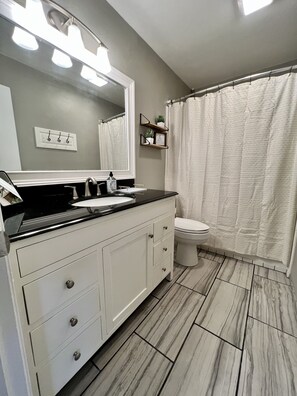 A bathroom with a white vanity, a mirror, a sink, a toilet, and a shower curtain. - *New* Welcome to the Cheerful 2 Bedroom Duplex (Tyler)