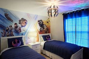 A bedroom with two beds, a nightstand, a lamp, and a wall mural of a space-themed movie.