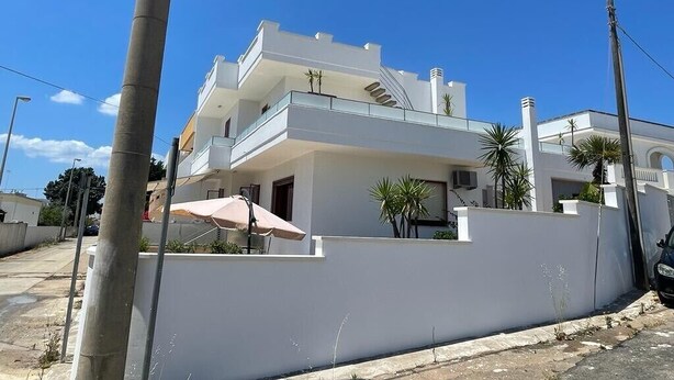 Ein modernes, zweistöckiges Haus mit Balkon, heller Fassade und einem kleinen Garten.