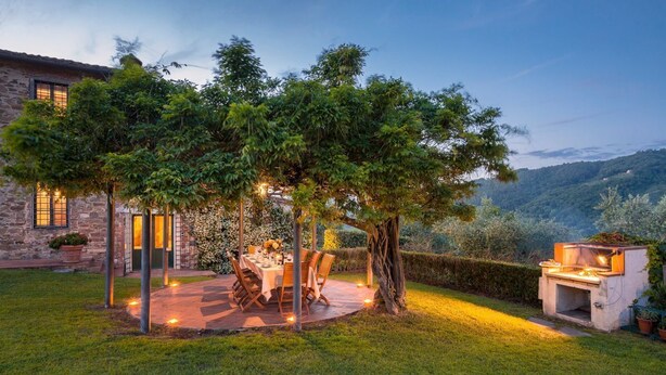 Un espace de restauration en plein air, avec une table et des chaises, entouré d’arbres et d’un bâtiment en pierre.