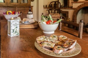 Ein Holztisch mit einer Schüssel frischem Gemüse, einer Platte geröstetem Brot mit Kräutern und einem Behälter mit nativem Olivenöl.