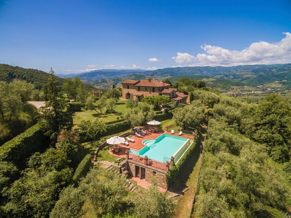 A large house with a swimming pool surrounded by lush greenery and a view of distant hills.