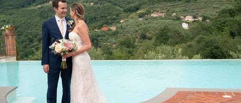A couple standing by a pool with a mountainous backdrop.