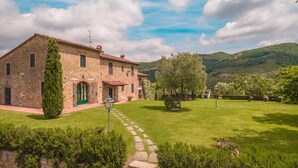 Un bâtiment en pierre avec une porte verte, entouré d’une pelouse bien entretenue et d’arbres.