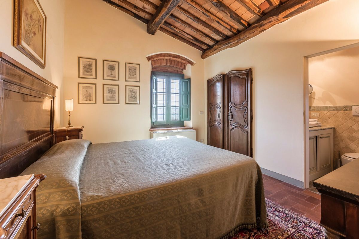 Een slaapkamer met een groot bed, houten meubels, een raam met groene luiken en lijstjes met foto's aan de muur.