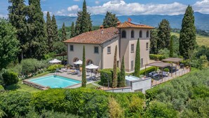 Una villa de dos pisos con piscina, mobiliario exterior y vistas a las montañas.